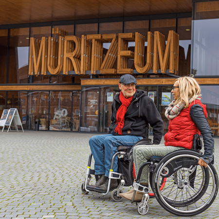 Zwei Rollstuhlfahrer stehen auf dem Vorplatz vor dem Haupteingang des Müritzeum.