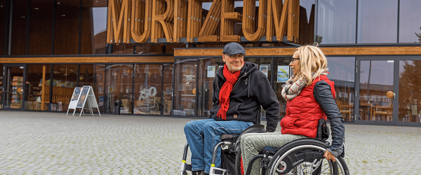Zwei Rollstuhlfahrer stehen auf dem Vorplatz vor dem Haupteingang des Müritzeum.